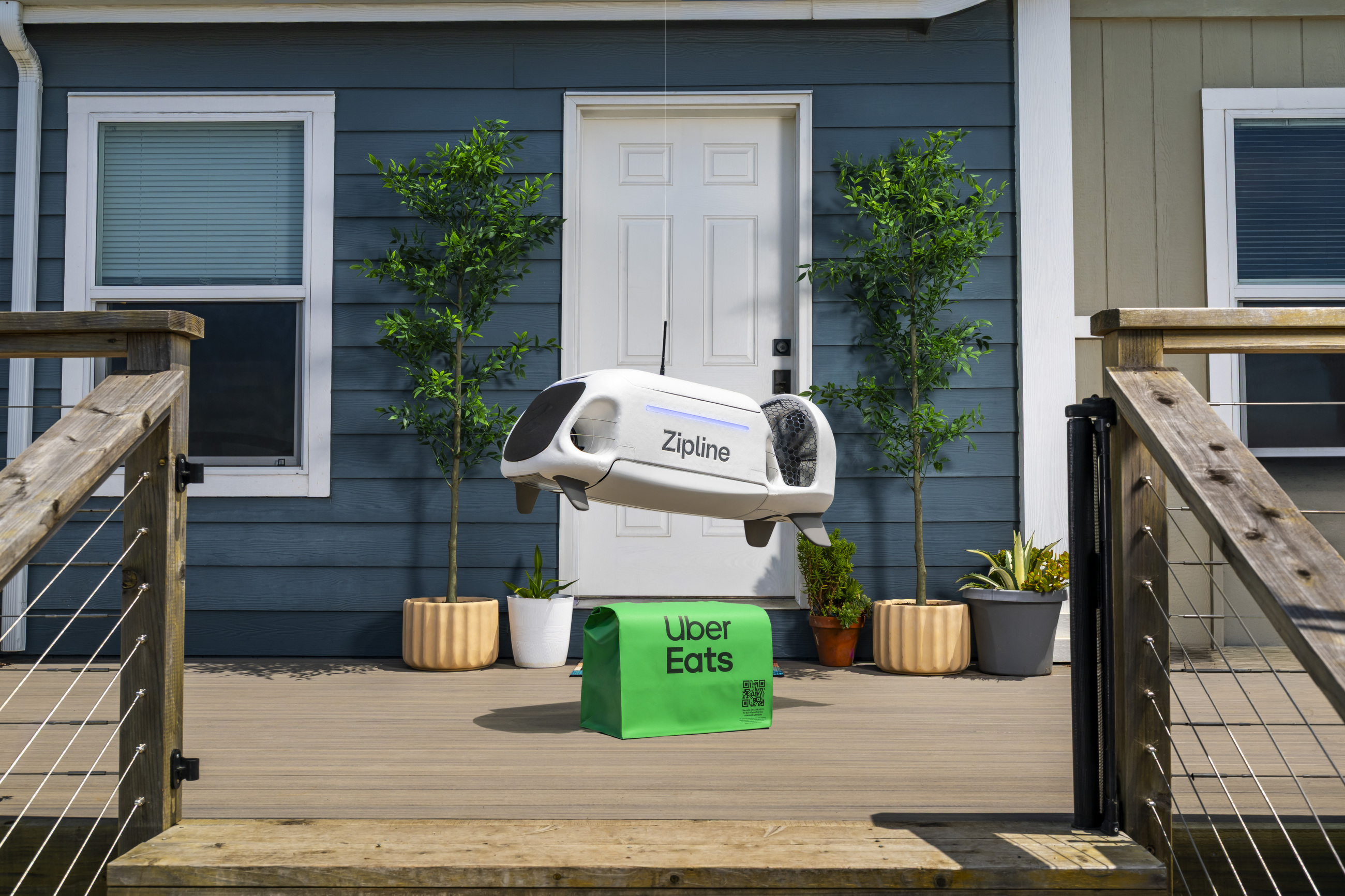 A Zipline delivery droid hovers at a house front door above an Uber Eats order bag on the deck.